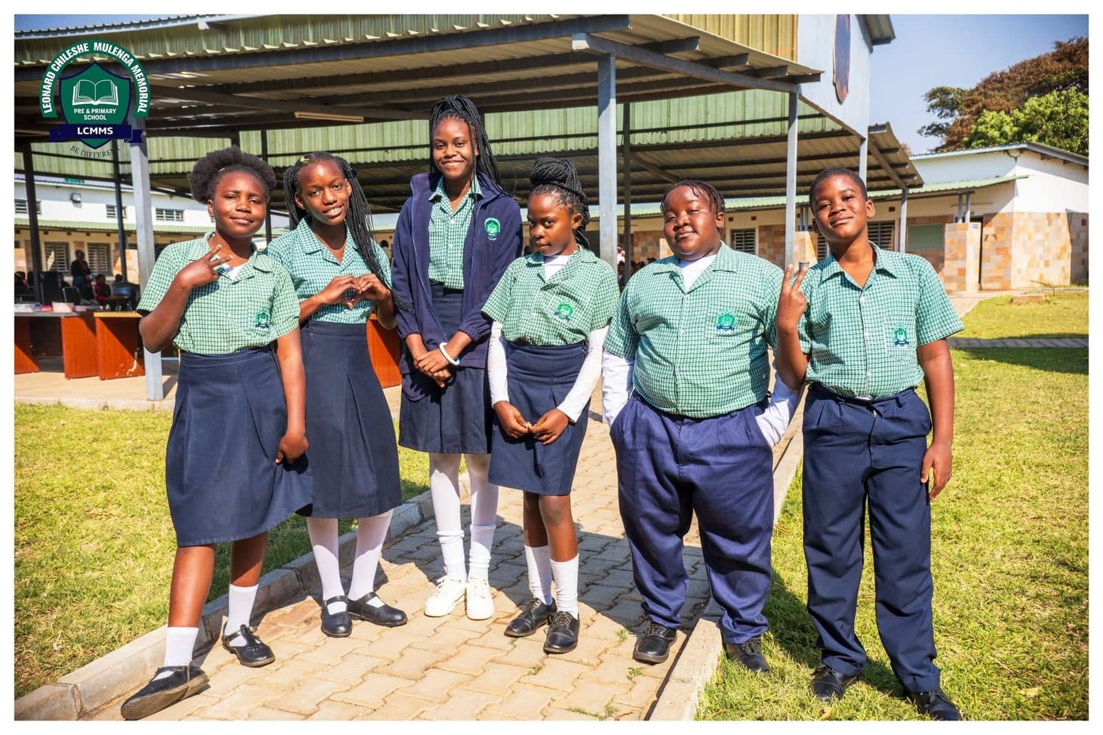Six pupils in green and navy uniforms standing together on the school grounds