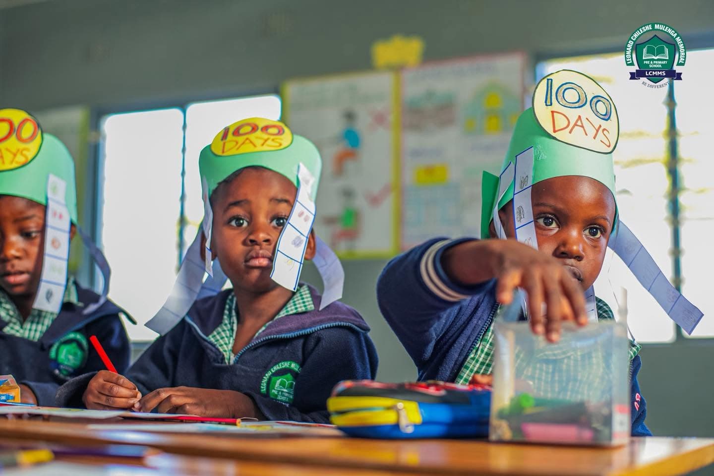 Learners in handmade celebration crowns sit with pencils and classroom materials