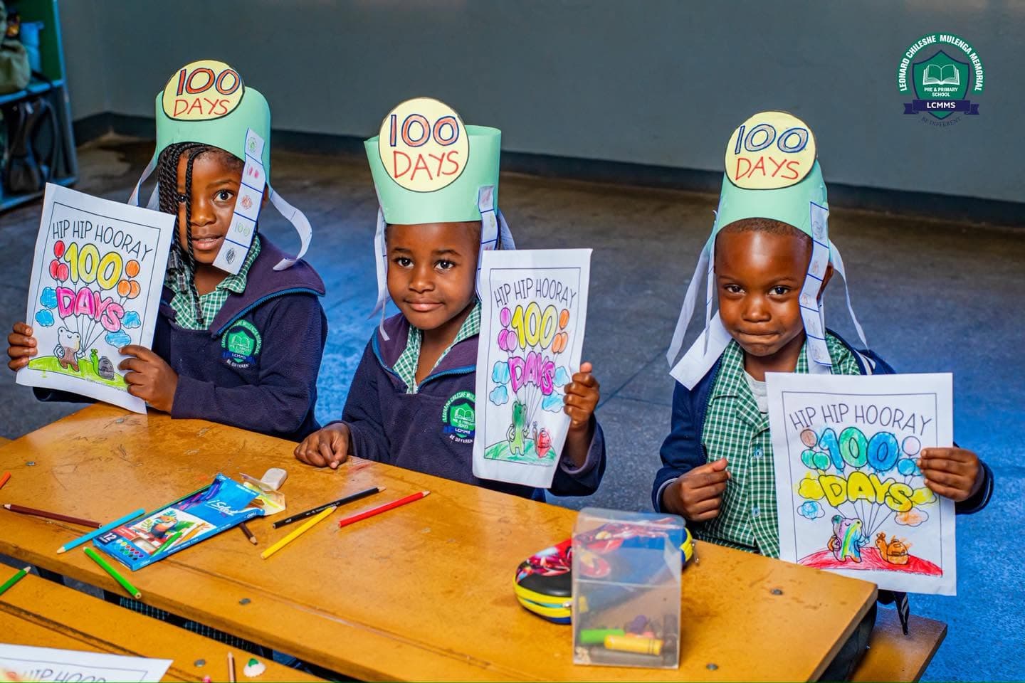 Three learners in 100 Days crowns hold up their celebration artwork