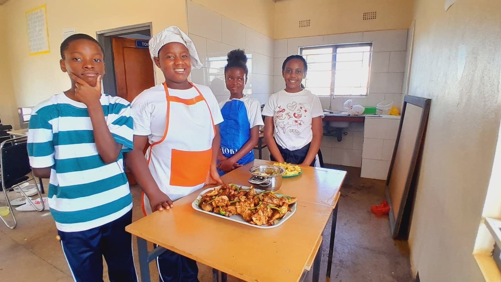 Grade 7 learners in aprons stand beside a platter of food they have prepared