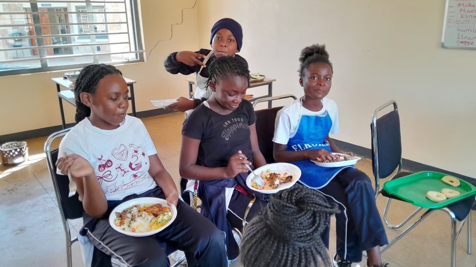Two Grade 7 learners hold plates of food beside their classmates
