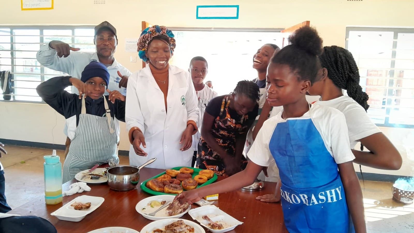 Learners in aprons present their cooking work around a classroom table
