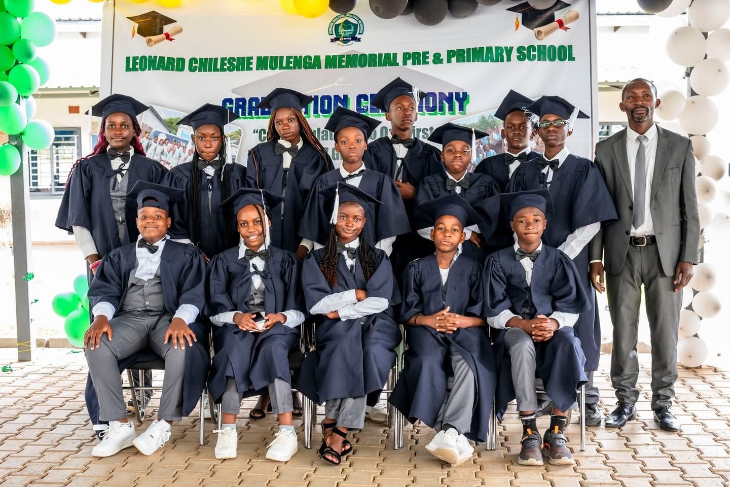 Grade 7 learners in navy graduation gowns pose with a staff member at the school graduation ceremony