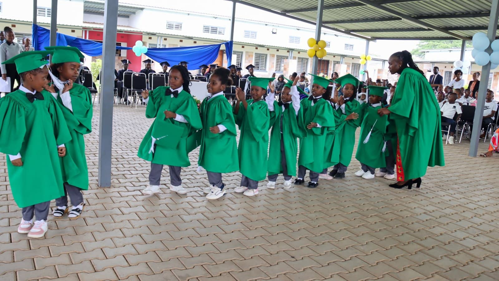 Young graduates in green caps and gowns gather under the covered courtyard for the ceremony