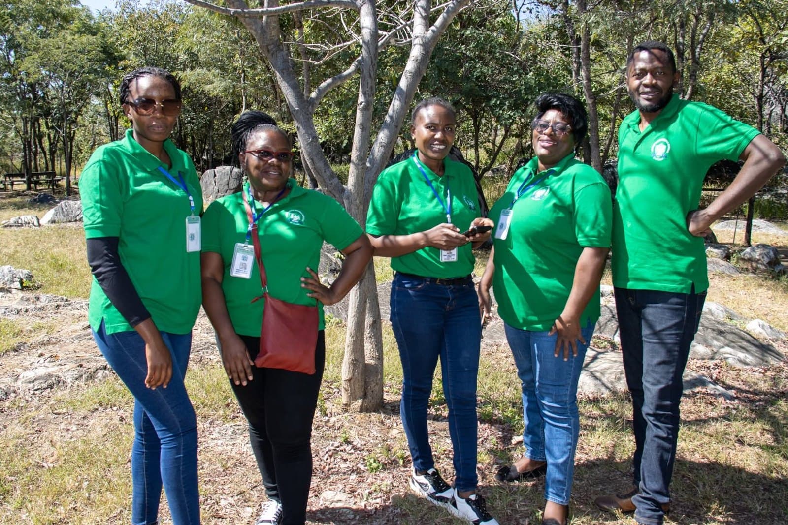 School staff in green shirts stand together among trees during the outdoor visit