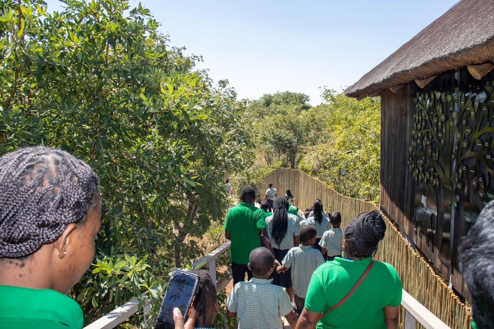 Learners and staff follow a raised walkway beside a thatched building at the park