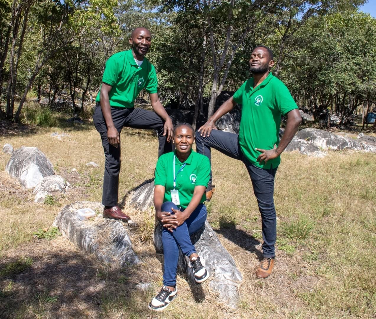 Three members of staff in green shirts pose beside rocks and trees during the park visit