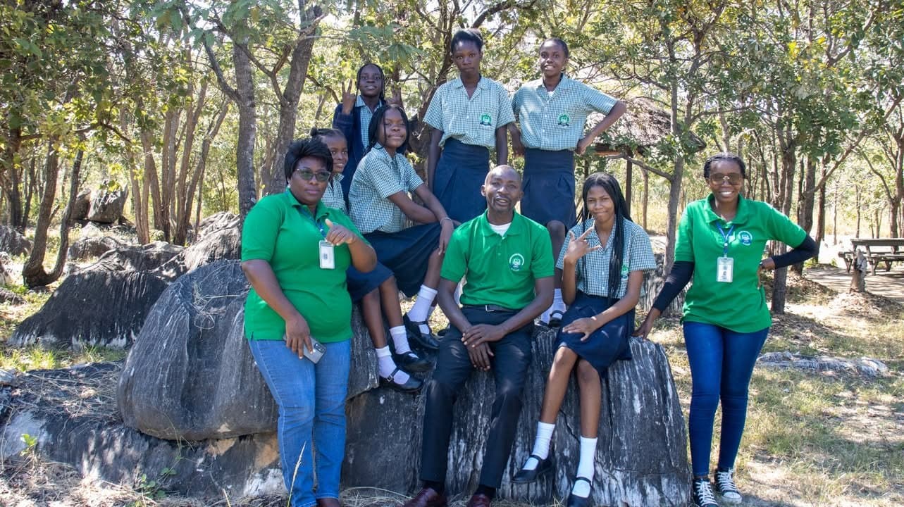 Learners and staff gather for a group photograph among rocks and trees
