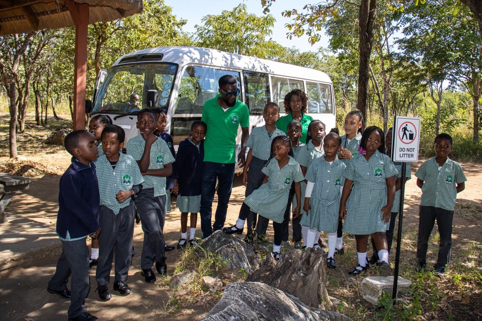 The school group stands together beside its transport in the park
