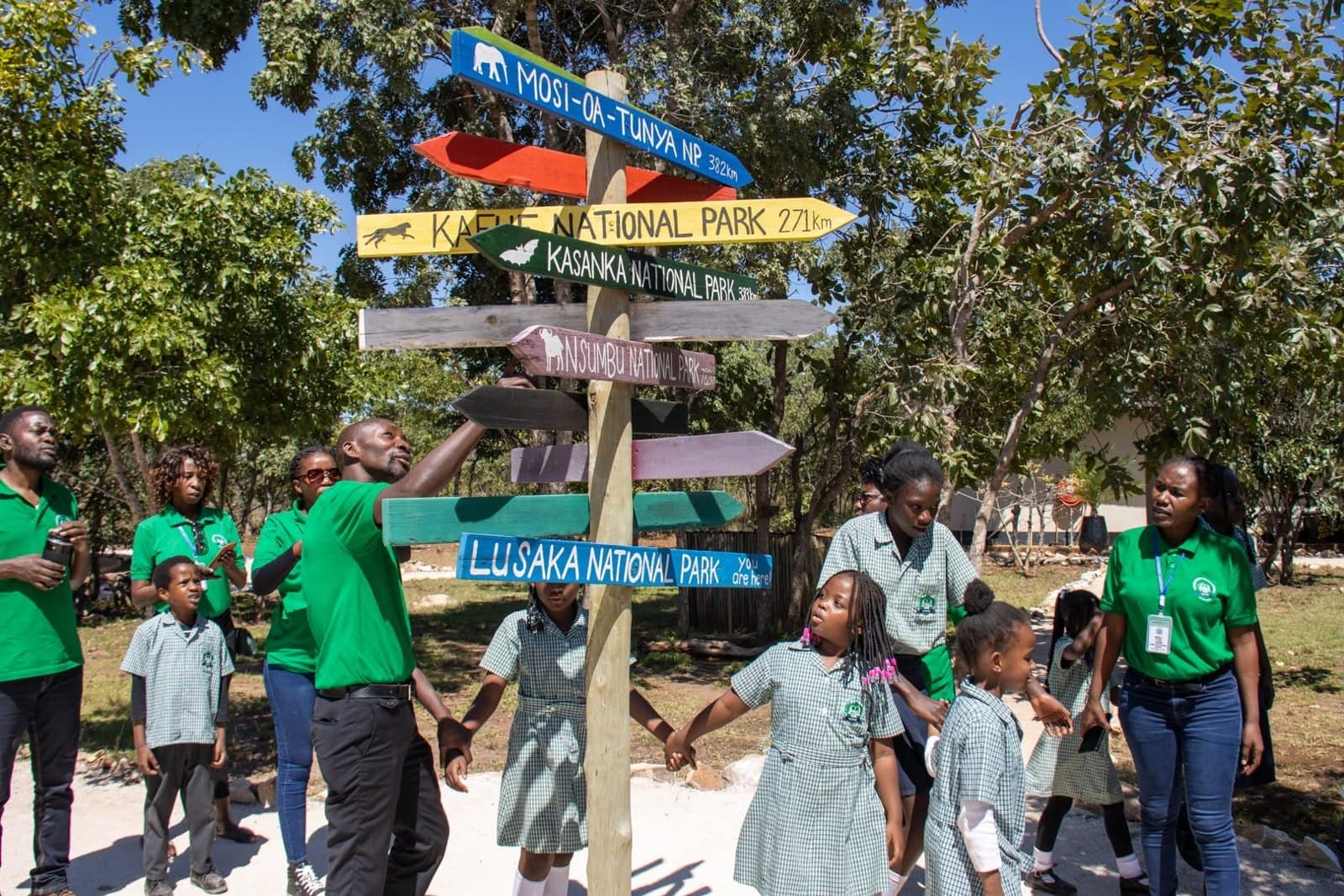 Learners and staff gather beneath a colourful directional sign at the wildlife education centre