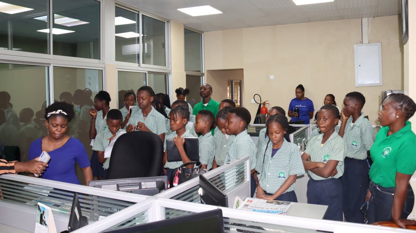 Learners and accompanying adults stand together between newsroom workstations