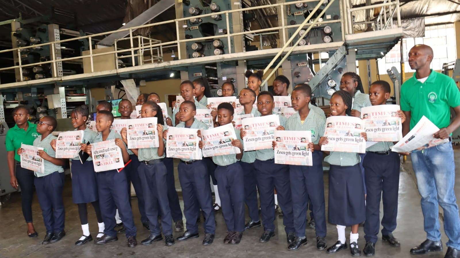Learners display their newspapers in front of the printing machinery