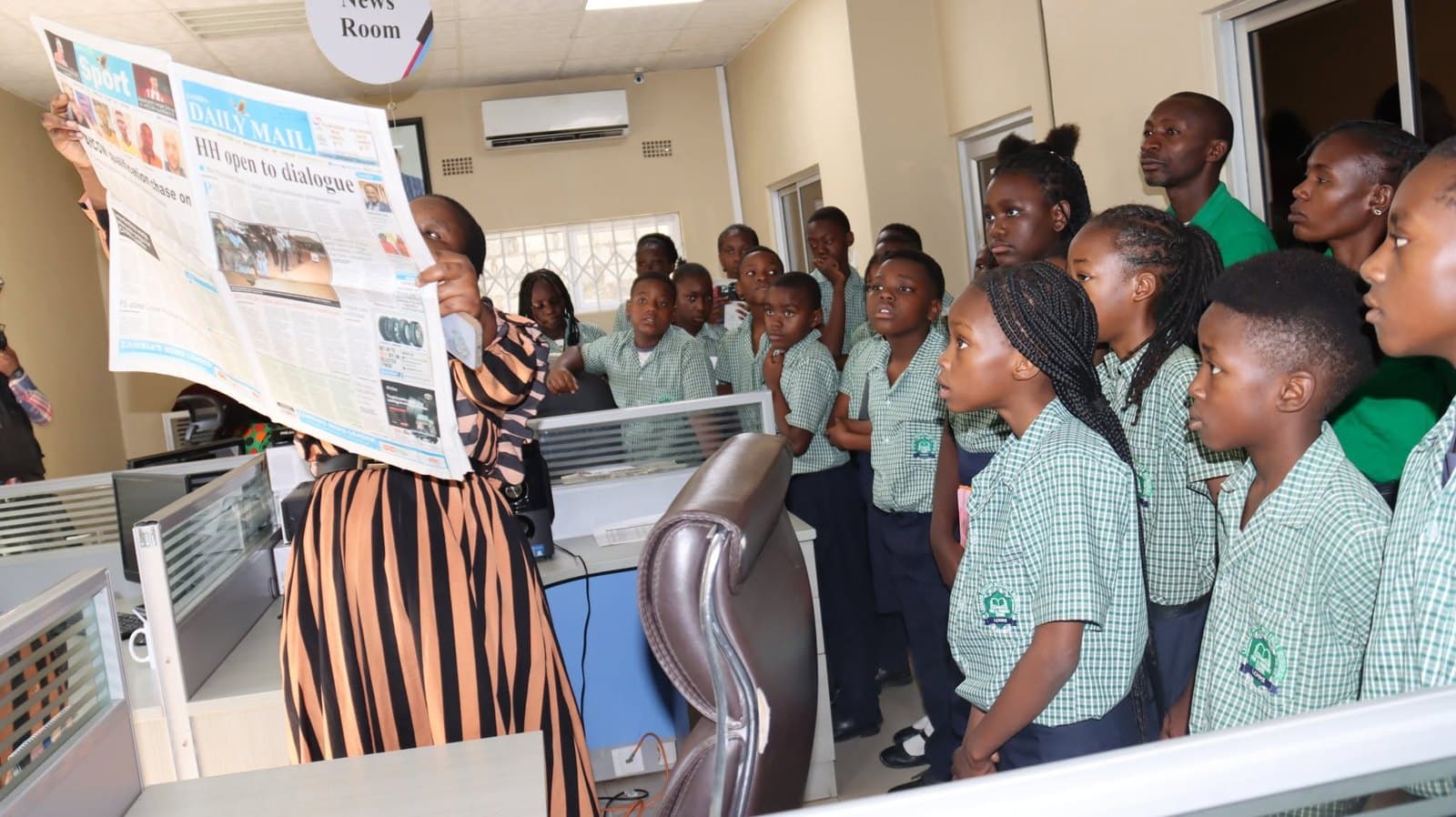 A member of the visiting group holds up an open newspaper for learners to see