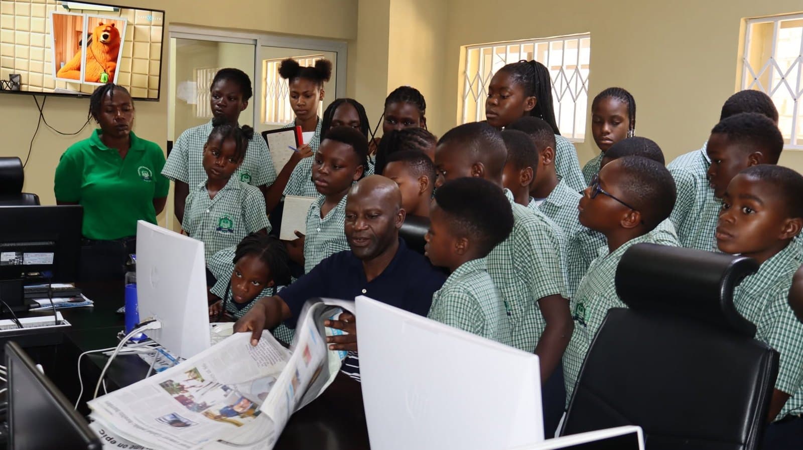 Learners look closely at a newspaper beside newsroom computer screens