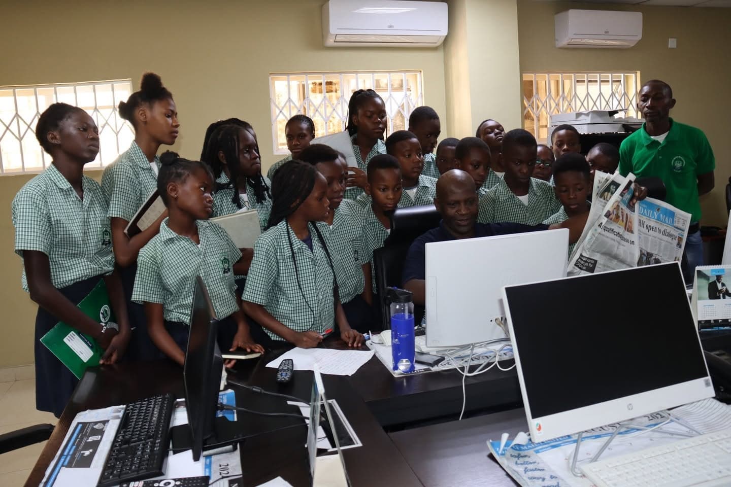 The school group listens beside a row of newsroom workstations