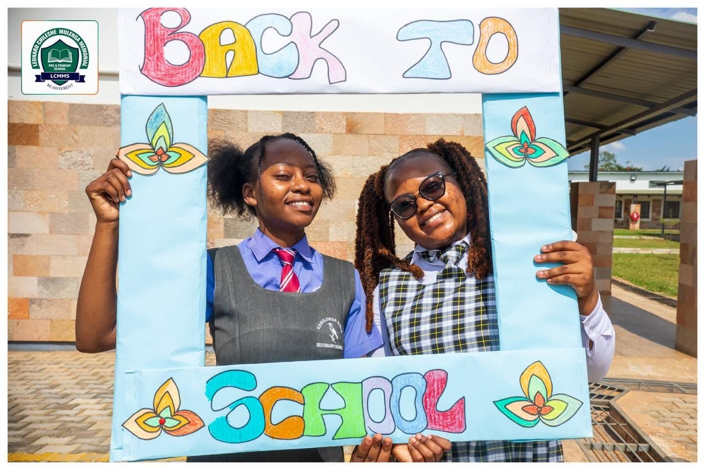 Two teachers in school uniform posing inside a colourful Back to School photo frame