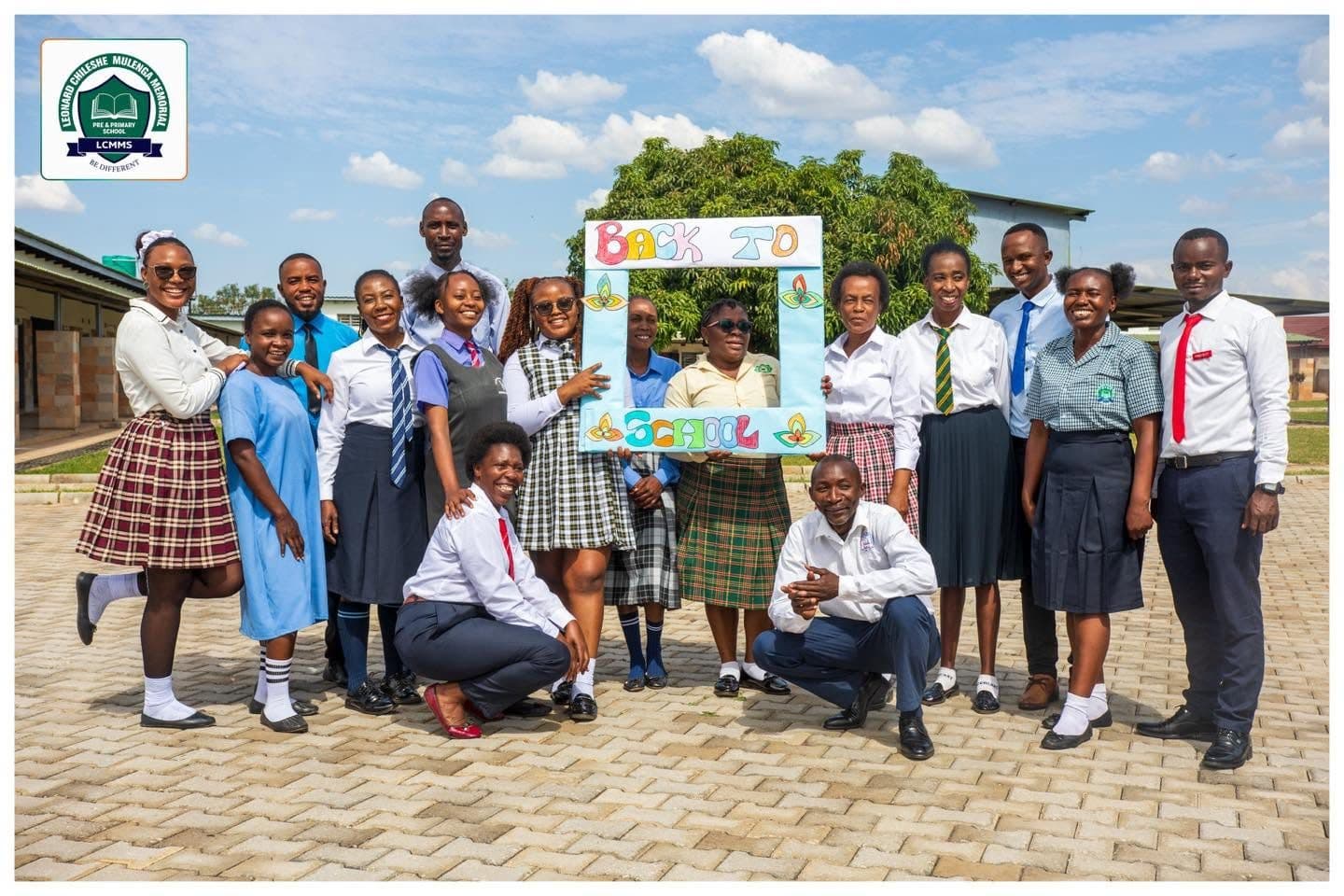 Staff dressed in school uniforms posing together on the paved courtyard