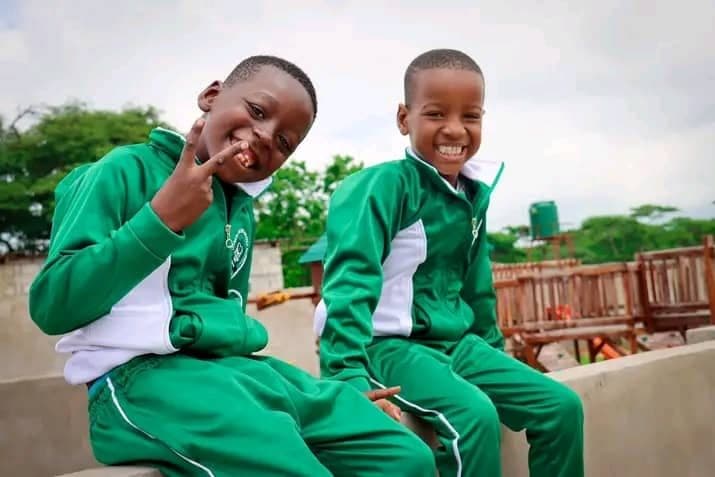 Two smiling pupils in green tracksuits sitting together outside