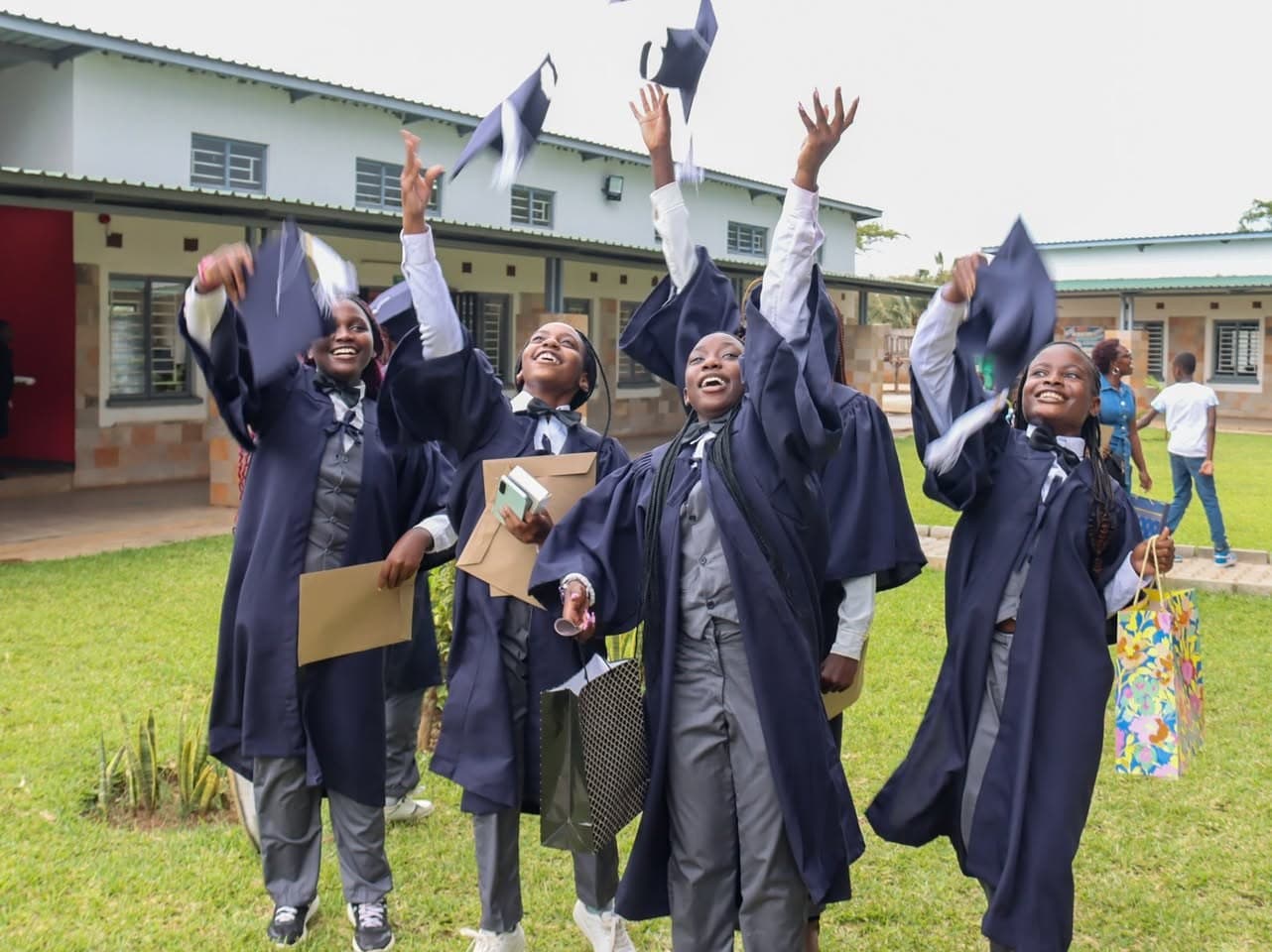 Grade 7 learners in graduation gowns throw their caps into the air on the school grounds