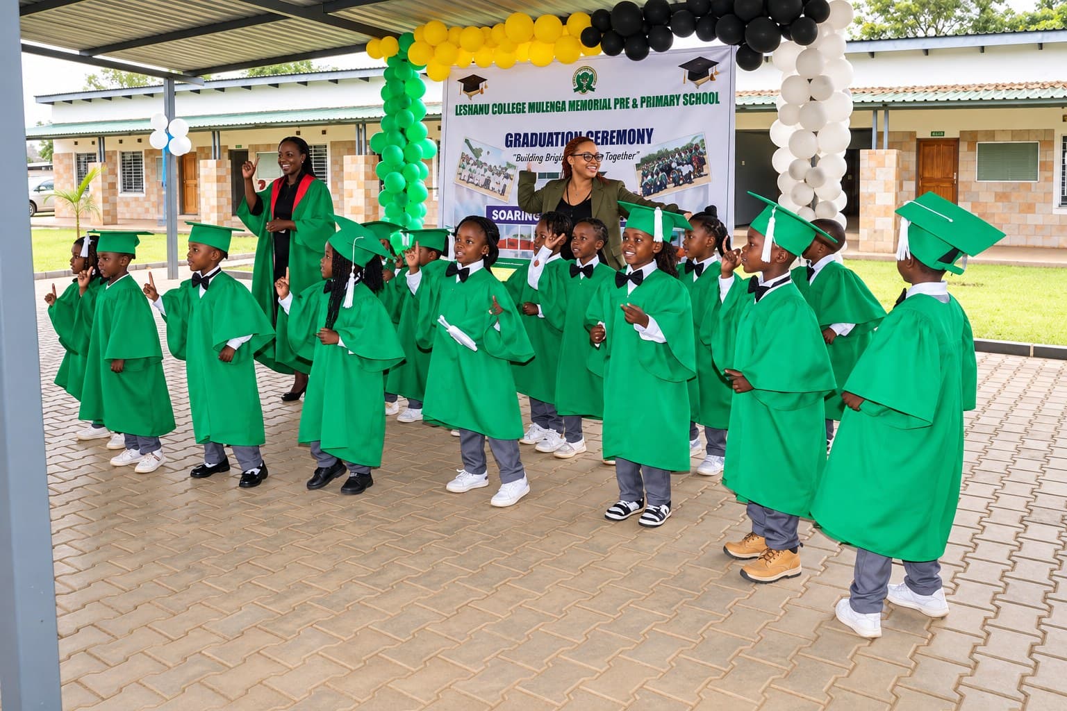 Reception graduates in green caps and gowns stand together beneath balloons at the graduation ceremony