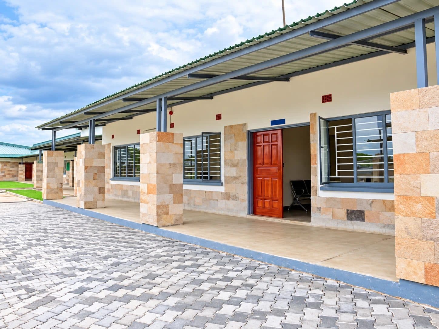 A classroom block with stone-clad pillars, a covered walkway and a red wooden door