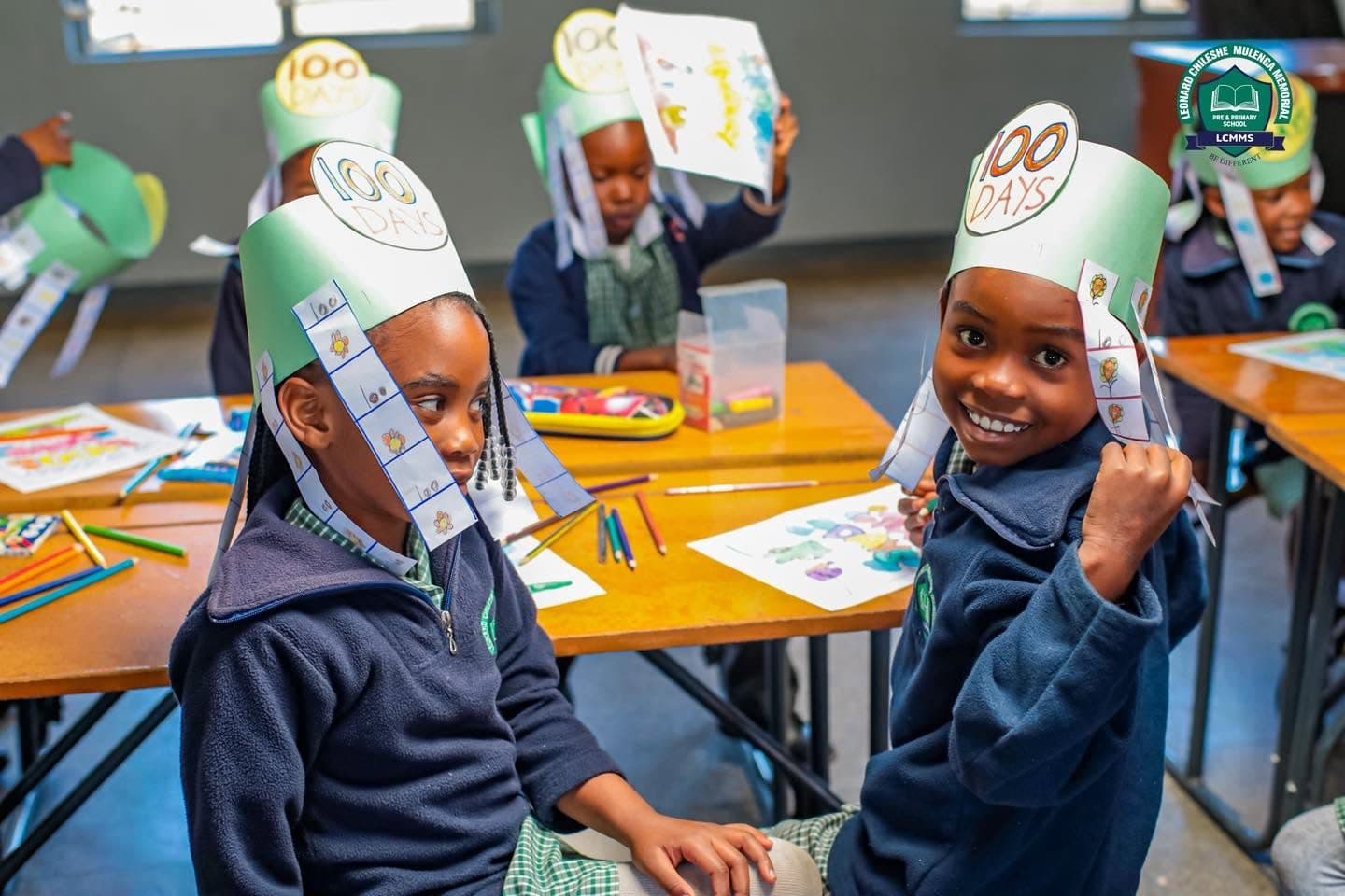 A smiling pupil in a 100 Days crown at a desk covered in drawings