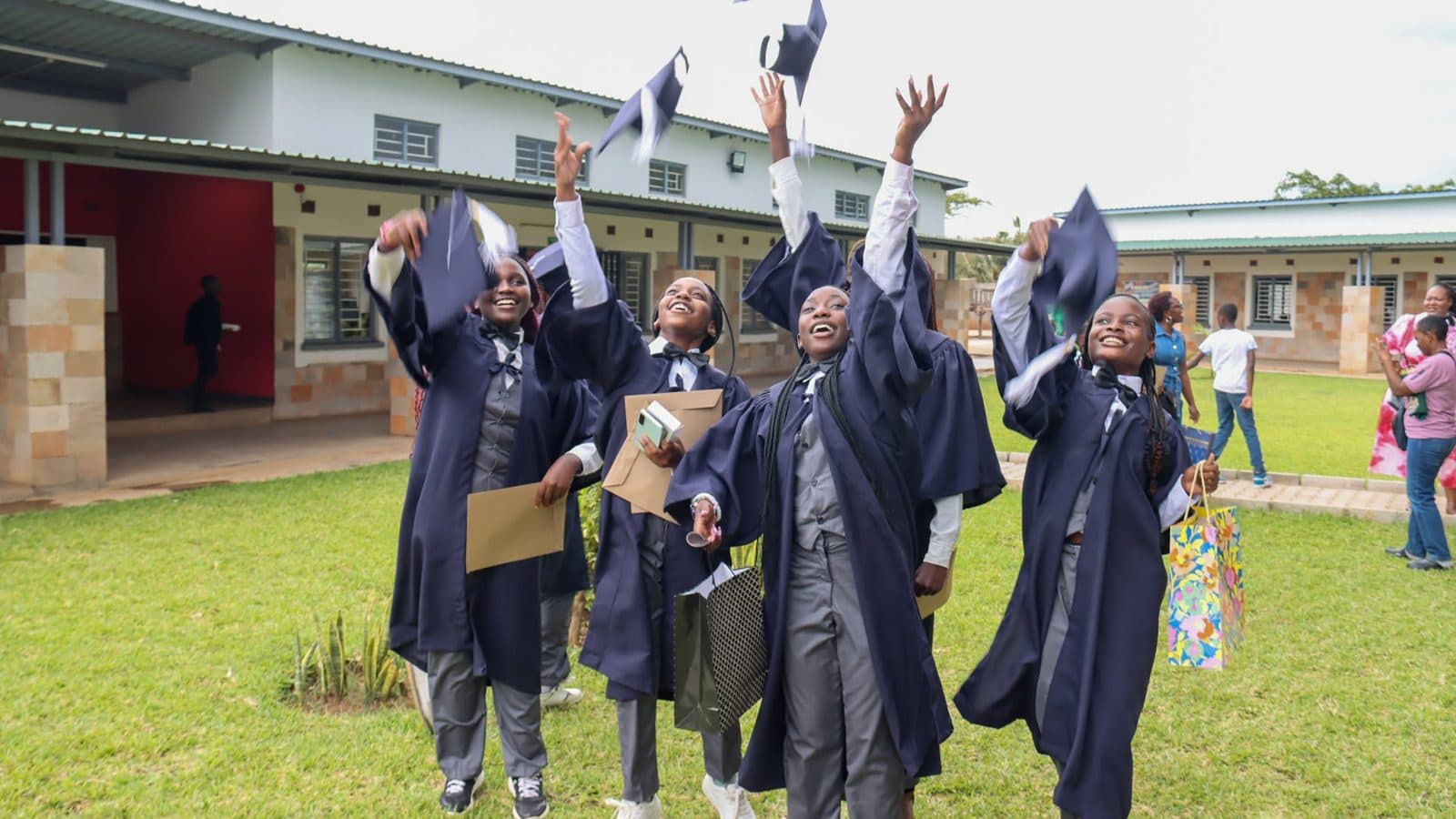 Grade 7 graduates in navy gowns throwing their caps in the air on the lawn