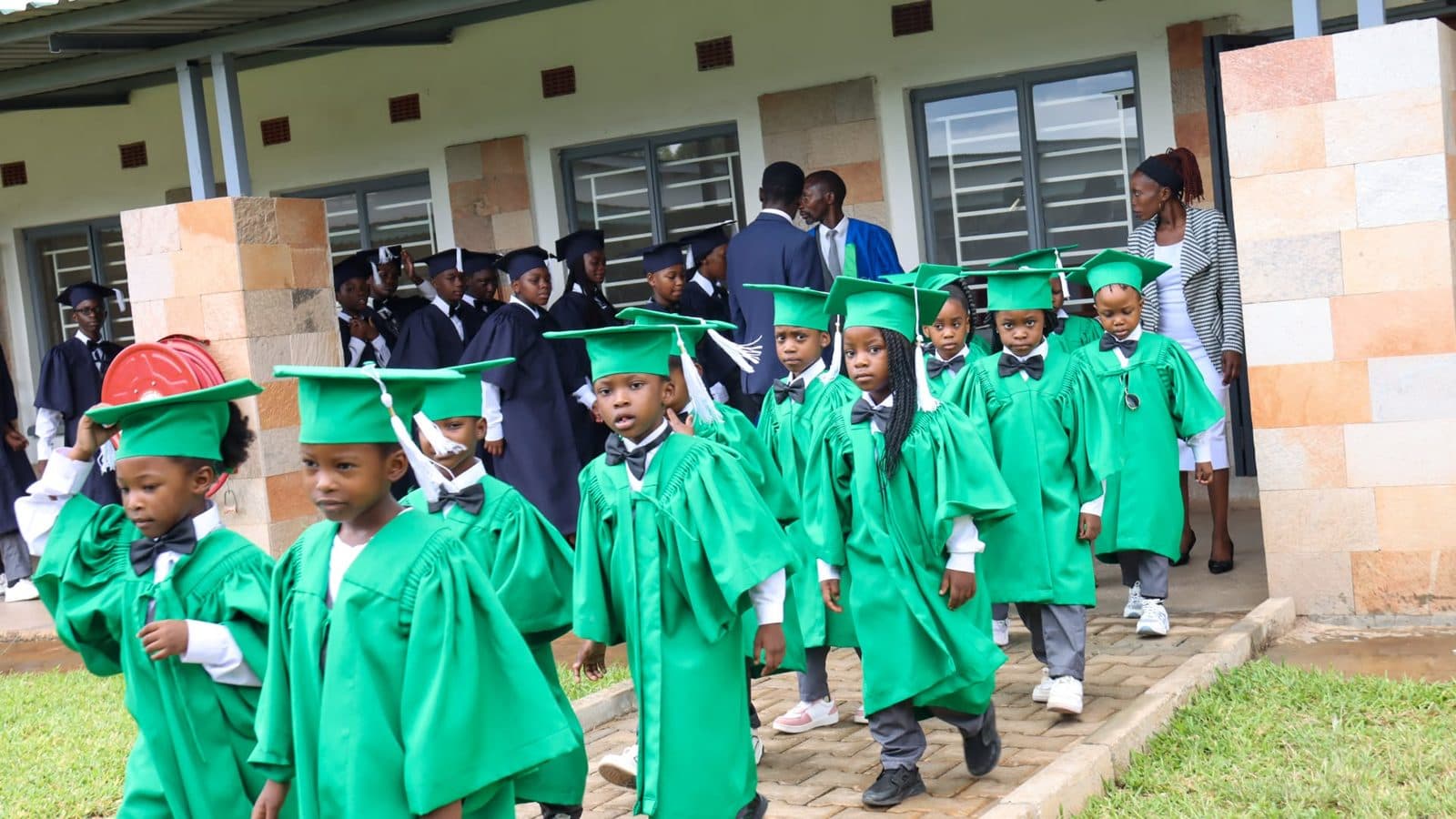 Young graduates in green caps and gowns walking out of a classroom block