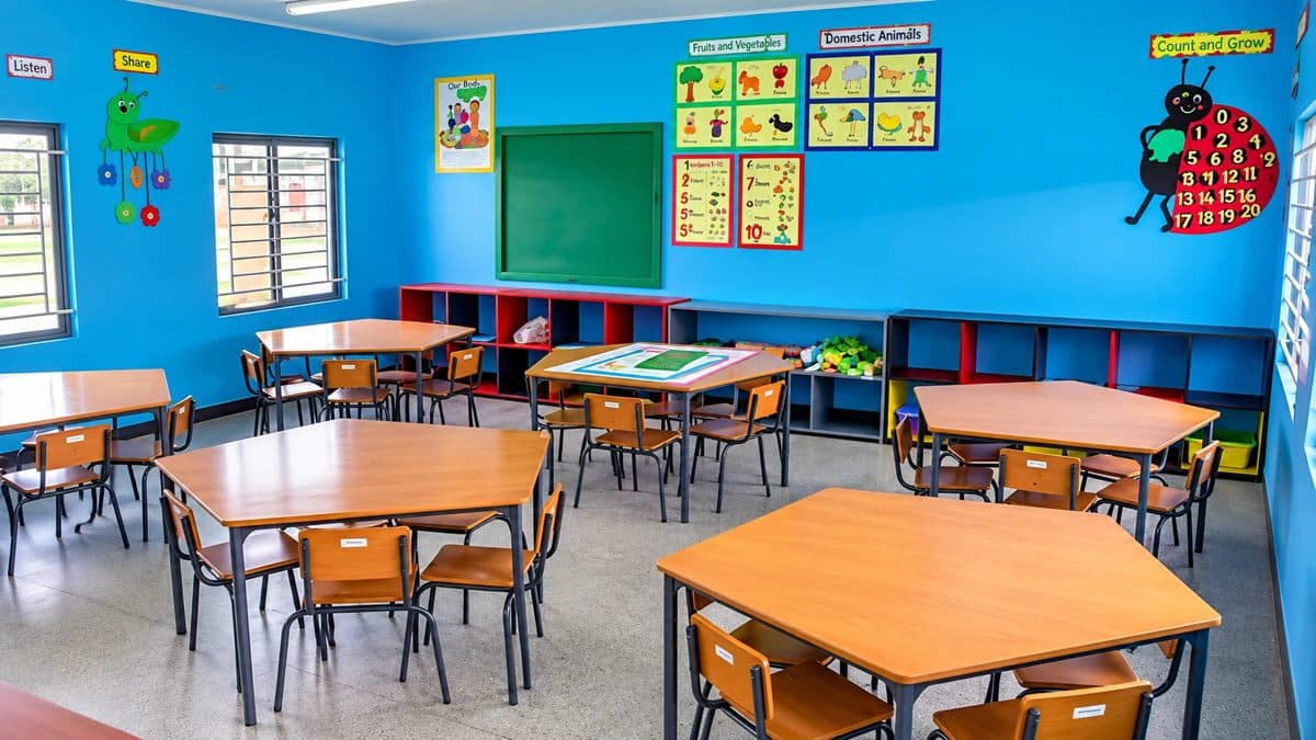 A bright blue early-years classroom with hexagonal tables, small chairs and learning charts