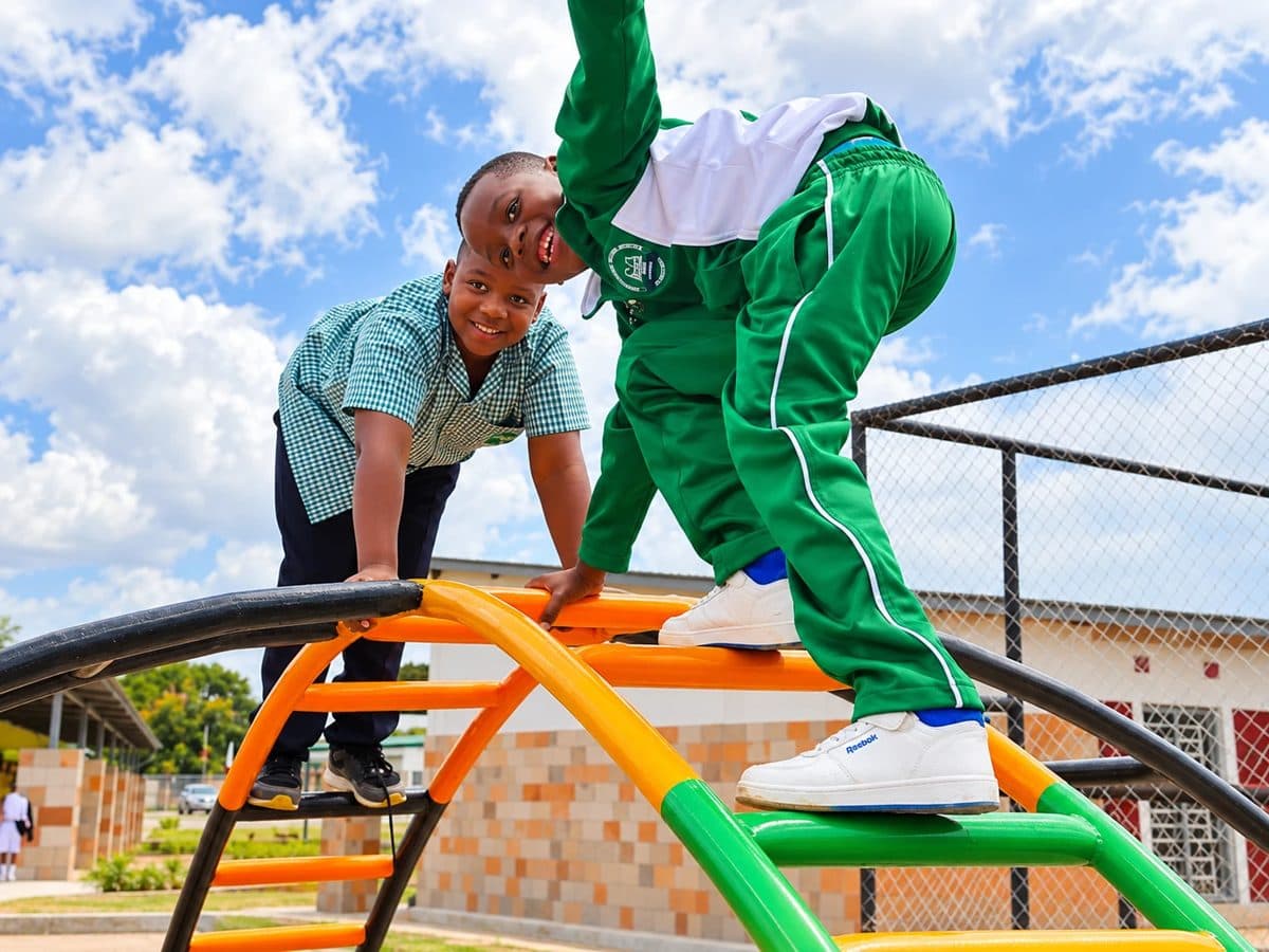 Two smiling pupils climbing the orange and green climbing frame on the playground